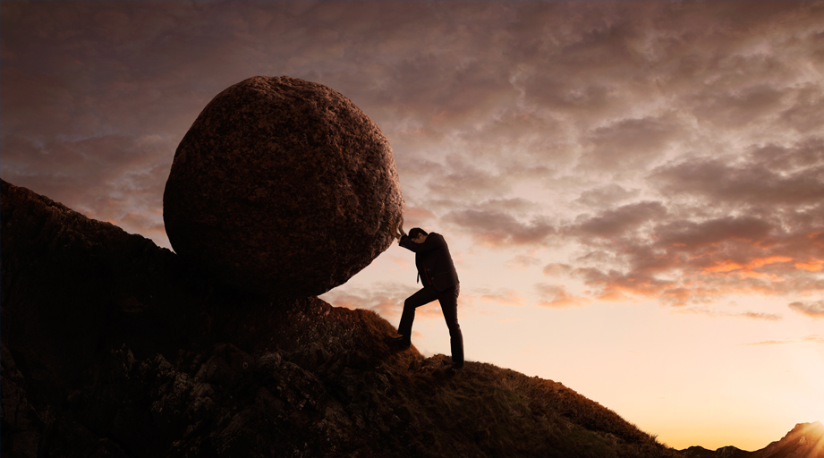 photo of man pushing large stone uphill