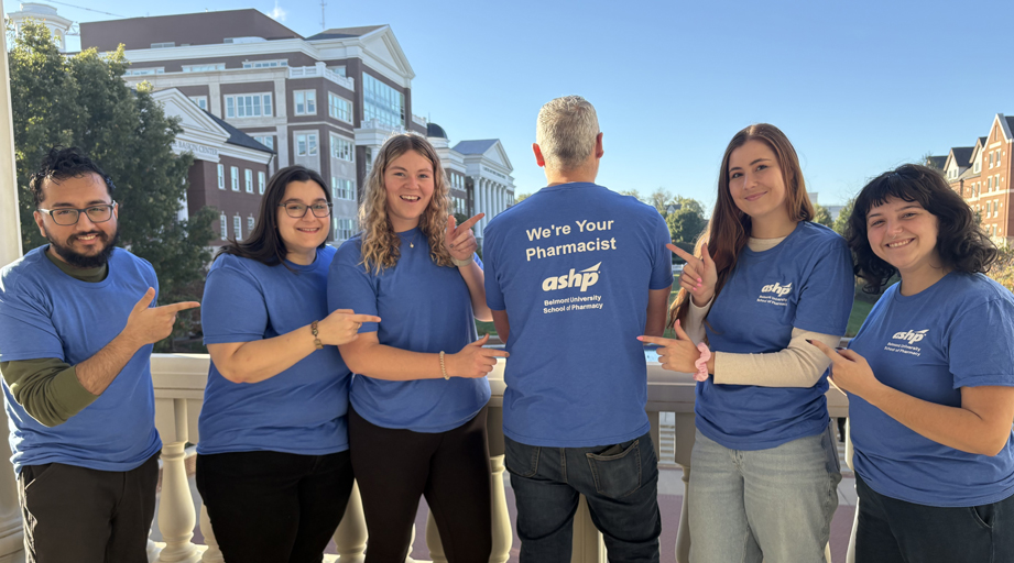 Belmont University School of Pharmacy students posing and pointing to back of another student, shirt says: We're Your Pharmacists - ASHP