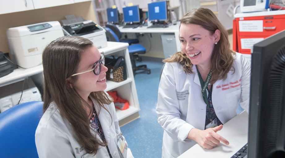two female pharmacists talking and smiling, seated at a workstation