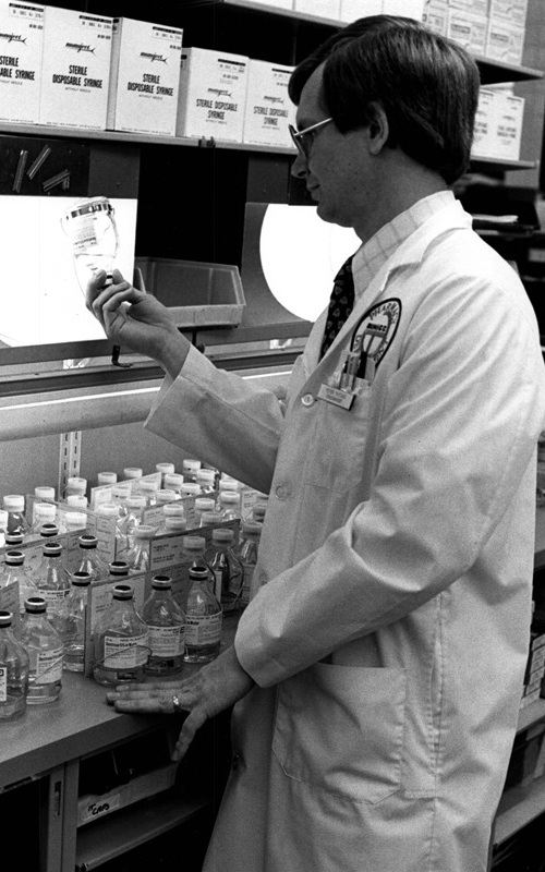 NIH pharmacist Peter L. Vaccari inspects IV solutions prepared at the Clinical Center pharmacy, 1983.