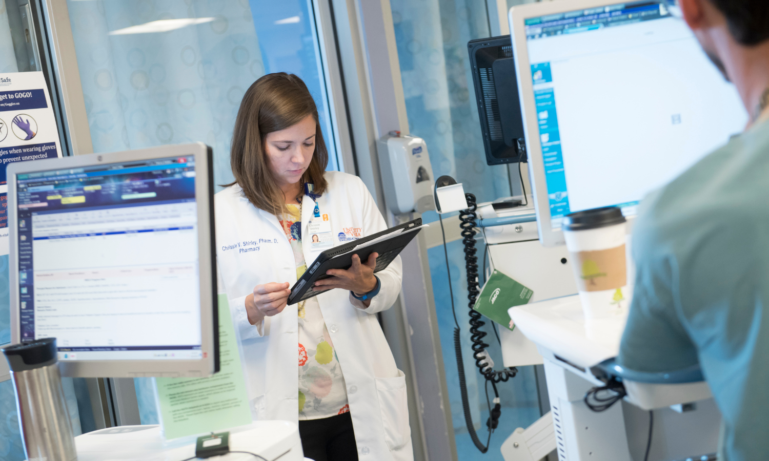 Pharmacist looking at her tablet in a health care setting while next to two computers